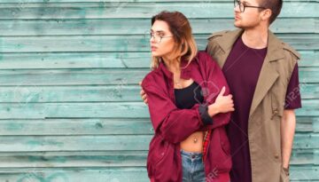 fashion couple in their glasses with burgundy clothes posing on a blue wooden wall