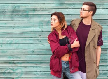 fashion couple in their glasses with burgundy clothes posing on a blue wooden wall