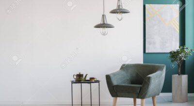 Stylish interior in white and green with armchair and teapot set on the table, modern lamps, a plant in a pot and a poster