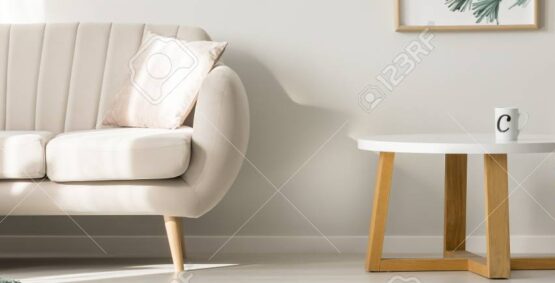 Round wooden table next to sofa with green blanket in simple living room interior with ladder