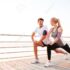 Athletic young couple doing stretching legs exercises together on the pier
